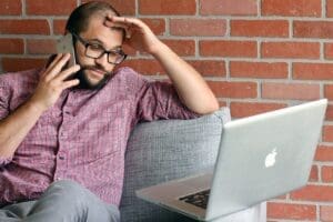 Man talking on phone while looking at laptop.