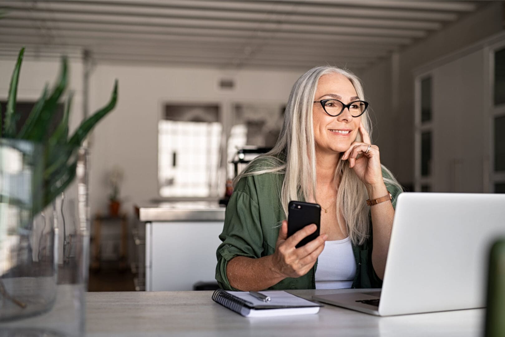 A woman sitting at a desk with a laptop and cell phone.